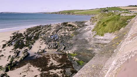 Coastal-area-in-county-Cork,-with-rocks-and-cliffs-and-sandy-beach-on-low-tide-and-sunny-day