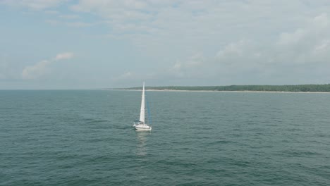 Aerial-establishing-view-of-a-white-sailboat-in-the-calm-Batltic-sea,-white-sailing-yacht-in-the-middle-of-the-boundless-sea,-sunny-summer-day,-wide-tracking-done-shot