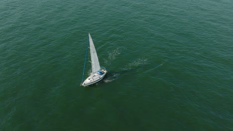 Aerial-establishing-view-of-a-white-sailboat-in-the-calm-Batltic-sea,-white-sailing-yacht-in-the-middle-of-the-boundless-sea,-sunny-summer-day,-wide-done-shot-moving-backward,-tilt-up