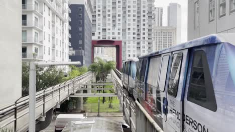 Toma-De-Gran-Angular-Del-Primer-Tri-rail-Alimentado-Con-Biodiesel-Que-Cruza-La-Estación-Con-Los-Edificios-Del-Horizonte-De-Miami-Al-Fondo