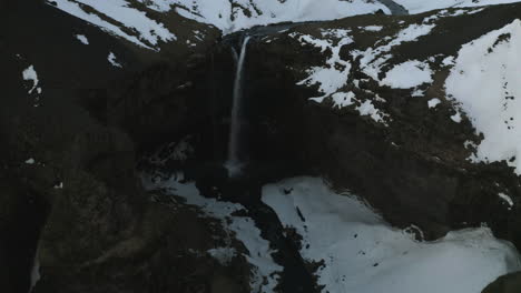 Aerial-view-tilting-away-from-the-snowy-Seljalandsfoss-waterfall,-winter-evening-in-Iceland