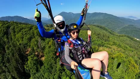 Woman-sits-in-harness-soaring-with-paraglide-tour-guide-above-epic-vibrant-mountain-valleys