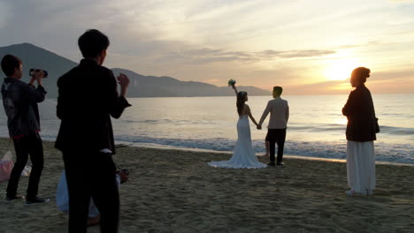 Young-married-couple-stand-and-pose-at-sunset-on-beach-as-directed-by-professional-photographers