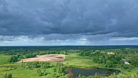 Stratonimbus-and-Stratus-Clouds-Over-Green-Vast-Countryside-Landscape-with-an-Aerial-Tilt-Down-Pull-Out-Shot,-Latvia