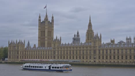 Boat-sailing-along-River-Thames-with-Palace-of-Westminster-in-background,-London