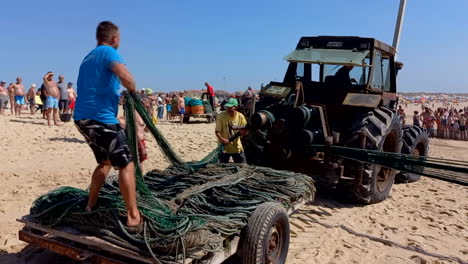 Tractor-Tirando-Redes-De-Pesca-De-Arrastre-O-Artes-Xávega-En-La-Playa-Durante-La-Temporada-De-Baño,-Pescadores-Enrollando-Las-Redes-Encima-Del-Tractor