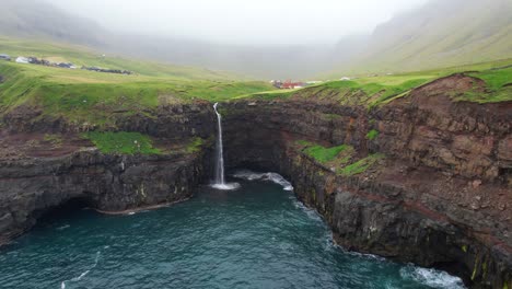 Mulafossur-ocean-waterfall-cliffs-and-foggy-Gasadalur-village-in-Vagar,-Faroe-Islands