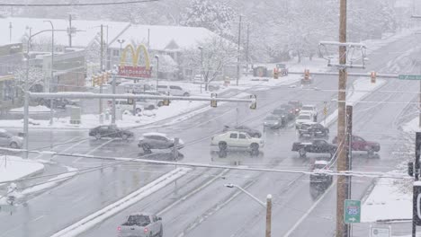 A-busy-intersection-with-cars-passing-from-left-to-right-and-others-waiting-during-a-cold-snowstorm-causing-slick-roads-in-December-of-2022-in-Midvale,-Utah