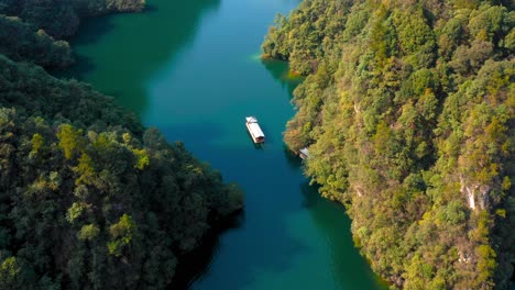 Drone-rear-view-tracking-follows-traditional-asian-boat-floating-peacefully-in-baofeng-lake-in-zhangjiajie,-Wulingyuan-Hunan-China