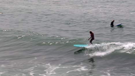 Aerial-View-Of-Male-Walking-Along-Board-Surfing-Wave