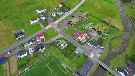 Football-pitch-by-river-in-Sandavagur,-a-lush-green-rural-Faroese-town