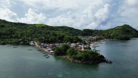 Cinematic-aerial-orbit-of-tropical,-coastal-village-with-a-white-lighthouse,-bangka-boats,-and-turquoise-ocean-waters