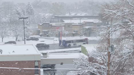 A-time-lapse-of-a-busy-intercity-road-during-a-cold-December-snowstorm-with-various-chain-restaurants-in-the-background-all-surrounded-by-snow-covered-trees-in-Midvale,-Utah