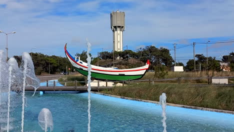 Boat-alluding-to-ancestral-art-at-the-entrance-roundabout-of-Praia-da-Tocha,-a-tribute-to-fishermen-and-Xávega-art,-with-water-fountains