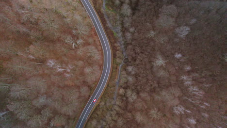 Aerial-view,-a-car-traverses-a-winding-road-next-to-a-river-in-a-mountain-valley-during-autumn