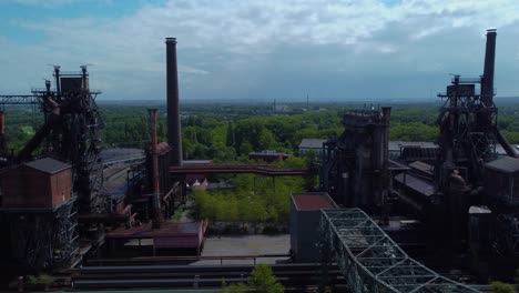 profile-view-moving-overview-of-well-aged-factory-in-the-middle-of-the-forest-in-Germany-plenty-constructions-metal-houses-coverings-power-plants-smokestacks-connected-together-well-managed-location
