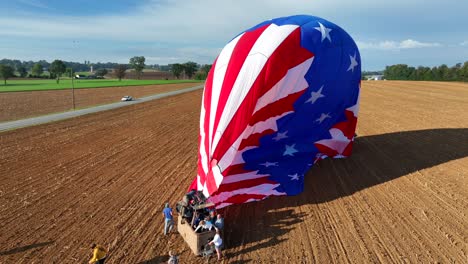 Aerial-view-showing-group-of-people-leaving-basket-of-Hot-Air-Balloon-with-american-flag-landing-on-rural-field-in-American-Countryside