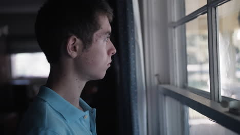 Cinematic-shot-of-a-sad-young-teenage-boy,-high-school-aged-young-man-with-depression-and-anxiety-looking-out-window-sadly