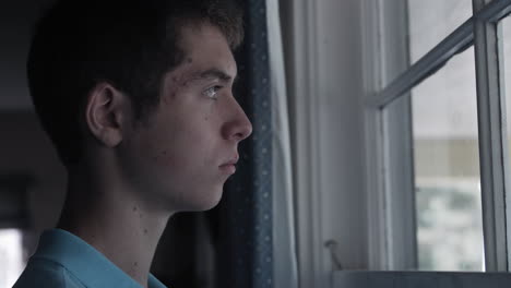 Cinematic-shot-of-the-face-of-a-sad-young-teenage-boy,-high-school-aged-young-man-with-depression-and-anxiety-looking-out-window-sadly