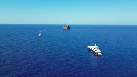 Boats-and-Strombolicchio-Volcano-Island-at-Stromboli,-Aeolian-Islands,-Sicily,-Italy---Aerial-4k