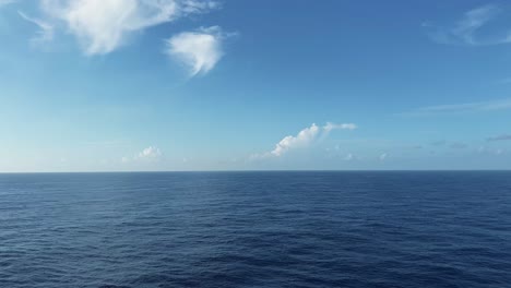 Panning-right-extreme-wide-shot-of-a-beautiful-empty-Caribbean-ocean-landscape-with-no-land-or-anything-in-site-and-calm-blue-water-below-on-a-warm-sunny-summer-day-with-a-few-clouds