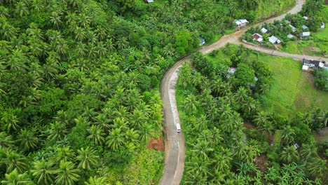 White-van-driving-through-empty,-scenic-road-in-the-middle-of-tropical-island-setting-with-lush-palm-trees-and-villages