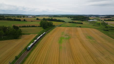 Train-on-railway-line-on-journey-through-fertile-Norwegian-countryside,-drone