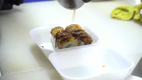 Slow-motion-shot-of-boxed-sushi-rolls-being-covered-with-soy-sauce-for-a-customer