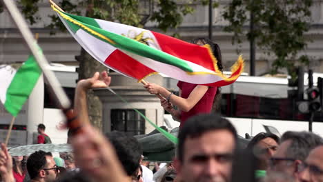 In-Zeitlupe-Schwenkt-Eine-Frau-Mit-Der-Aufschrift-„Freier-Iran“-Auf-Ihrem-Gesicht-Eine-Iranische-Flagge-Während-Einer-Protestkundgebung-Auf-Dem-Trafalgar-Square-Anlässlich-Des-Einjährigen-Todestages-Von-Mahsa-Amini