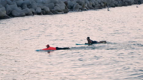 Instructor-De-Surf-Junto-Con-Su-Estudiante-Remando-En-El-Agua-Mientras-Está-Acostado-En-Una-Tabla-De-Surf-En-Sokcho,-Corea-Del-Sur