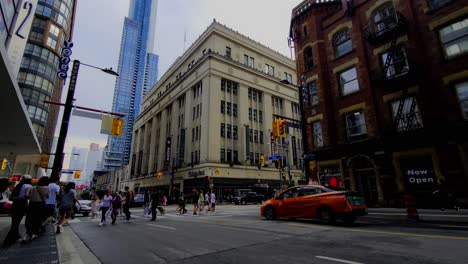 Fußgänger-In-Yonge-Und-College-In-Der-Innenstadt-Von-Toronto-übervölkern-Gehwege-Und-Fahrradkuriere-Bevölkern-Radwege,-Um-Lebensmittel-Und-Pakete-Auszuliefern.-Vintage-Gebäude-Im-Vordergrund,-Moderner-Hintergrund