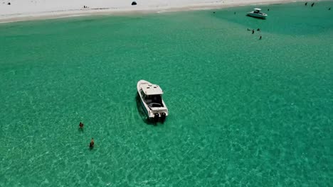 Top-view-of-boat-yatch-in-Green-crystal-clear-waters,-Blue-skies,-and-white-sands,-at-Shell-island-on-Florida’s-Emerald-Coast