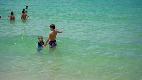 Happy-kid-playing-in-the-water-of-sea-while-wearing-a-colorful-swim-ring-life-jacket-on-summer-day