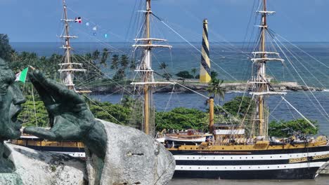 Drohnenaufnahme-Zeigt-Statue-Im-Hafen-Von-Santo-Domingo-Mit-Angedocktem-Italienischen-Trainingsschiff-Namens-Amerigo-Vespucci