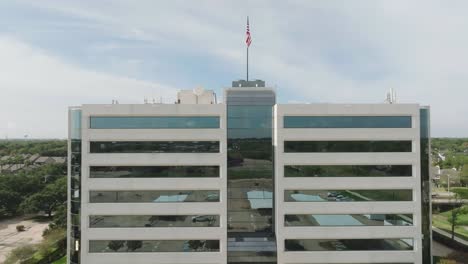 An-aerial-view-of-a-Contemporary-multi-story-office-building-with-an-American-flag-on-the-roof-waving-gently-in-the-breeze-in-Houston-Texas