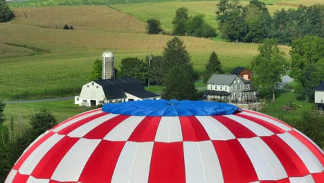 Drone-shot-revealing-farmland-of-Lancaster-County-through-American-flag-hot-air-balloon,-Pennsylvania,-USA
