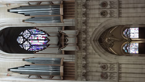 Vertical-View-Of-People-Walking-At-The-West-End-Of-Ulm-Minster-With-Organ-And-Stained-Window-In-Germany