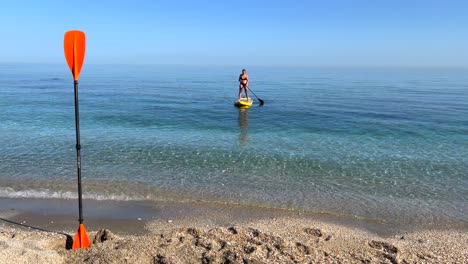 Chica-Surfeando-Lentamente-En-Charcos-En-El-Mar-En-Nerja-Málaga,-Poniéndose-De-Pie-En-Un-Charco-En-Un-Día-Soleado-En-España,-Divertida-Actividad-Vacacional,-Deportes-Acuáticos-De-Aventura,-Toma-Estática-De-4k