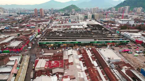 Vista-Aérea-Del-Establecimiento-De-La-Vega-Central,-El-Principal-Mercado-De-Comestibles-De-Santiago-De-Chile,-Que-Rodea-Casas-Empobrecidas-Con-Techos-De-Zinc.