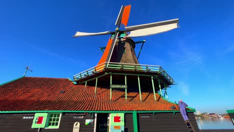 Standbild-Einer-Windmühle-Und-Eines-Mannes-In-Lila-Overall,-Der-Auf-Dem-Dach-Arbeitet