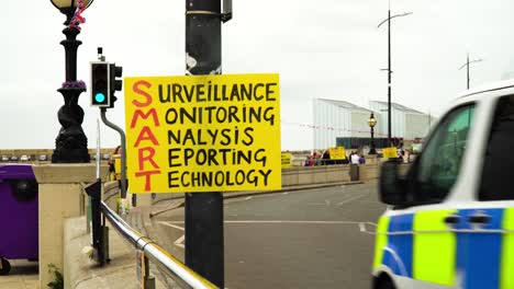 concerned-citizens-posted-plenty-of-signs-to-awaken-people-from-how-they-being-monitored-by-a-smart-technology-in-small-sand-other-sea-side-town-police-van-drives-by-and-other-cars-cloudy-weather