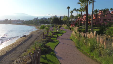 Vista-Aérea-Del-Hermoso-Sendero-Para-Caminar-Al-Atardecer-En-La-Playa-De-Estepona-Con-Palmeras-Junto-Al-Mar-En-Málaga,-España,-Destino-Perfecto-Para-Vacaciones-Familiares,-Toma-De-4k