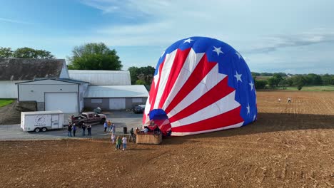 Aerial-backwards-shot-showing-group-of-people-after-flying-hot-air-balloon-with-American-flag-pattern-in-Amish-Country,-Pennsylvania