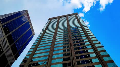 Yonge-and-Bloor-downtown-Toronto-bottom-to-top-view-RBC-and-CIBC-building-mirroring-each-other-on-a-sunny-day-as-white-and-gray-clouds-move-in-at-a-worms-eye-view