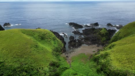 Aerial-view-of-idyllic-coastal,-sharp-rocks,-and-lush-hills-facing-turquoise-ocean-bay-in-Catanduanes,-Philippines