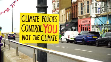 very-visible-yellow-sign-next-to-road-to-raise-awareness-about-climate-policies-controlling-the-people-but-not-the-climate-hanging-next-to-a-road-for-all-passing-drivers-to-see-this-message-cloudy-sky