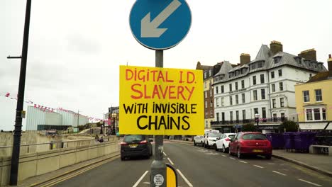 Cartel-Amarillo-Muy-Visible-De-Los-Manifestantes-Colgado-En-Un-Poste-De-Luz-En-Medio-Del-Papel-Con-Un-Mensaje-Sobre-Cómo-La-Identificación-Digital-Es-Una-Esclavitud-Con-Cadenas-Invisibles-Al-Tener-Un-Chip-Dentro-De-Nuestra-Mano-Derecha