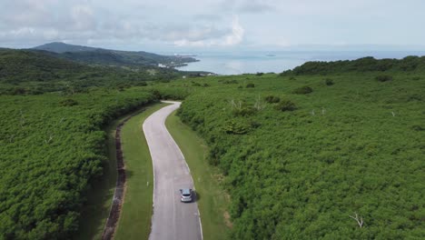 Drone-shot-of-a-car-driving-along-forest-road-in-a-tropical-island