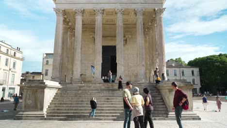 very-beautiful-architectural-stone-building-with-columns,-a-hexastyle-roman-temple,-"the-square-house"-famous-for-heritage,-in-a-town-in-the-south-of-France-with-people-in-front,-many-steps