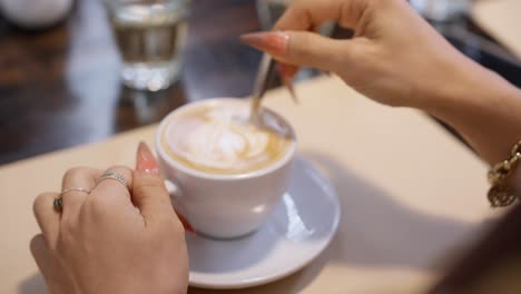 Nahaufnahme-Der-Hand-Eines-Schönen-Asiatischen-Mädchens,-Das-Zucker-In-Einer-Tasse-Kaffee-Rührt-Und-Sich-Darauf-Vorbereitet,-Den-Geschmack-Zu-Genießen